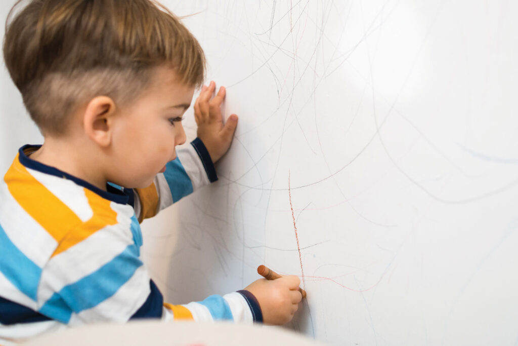 young Child Drawing On A Wall With Crayon