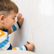 young Child Drawing On A Wall With Crayon