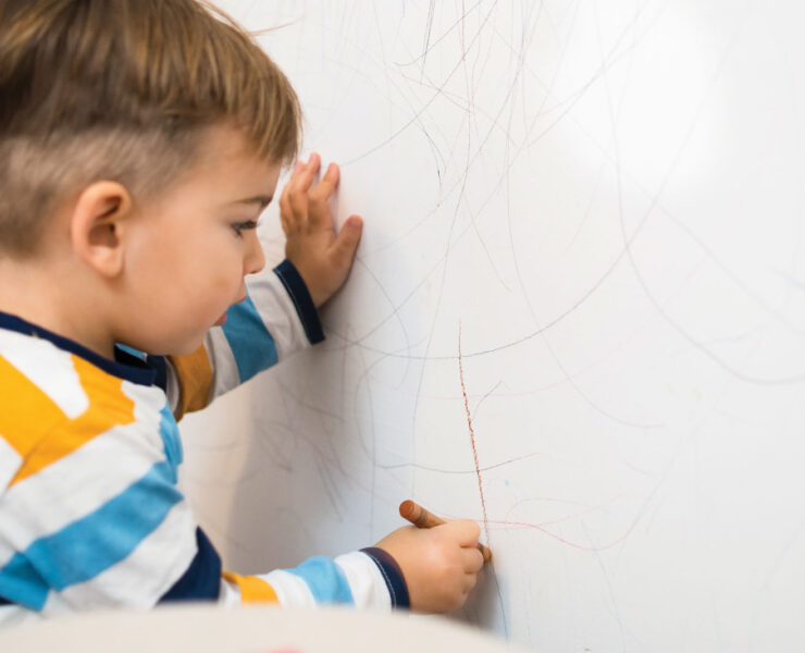 young Child Drawing On A Wall With Crayon