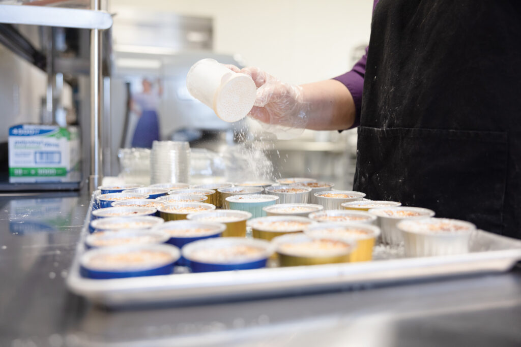 Owner Jean Nicklas Dusts Powdered Sugar Over A Tray Of Gooey Butter Cakes