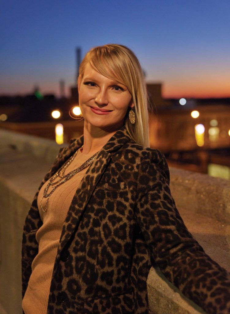 smiling at the camera. A sunset sky and city lights create a warm background.