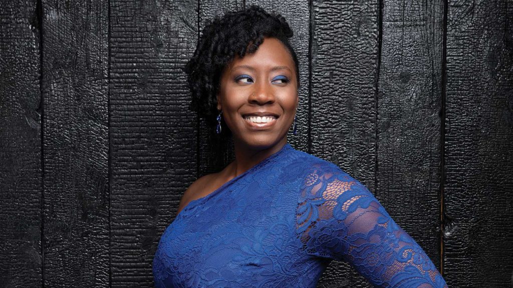 wearing a blue lace one-shoulder dress. They are posed against a dark