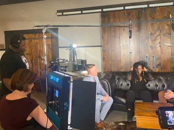 Two people filming and interviewing three people sitting on a couch with large wooden sliding barn doors behind them