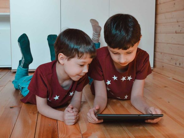 Two young boys are looking at the digital tablet to illustrate this article about online internet safety for kids.
