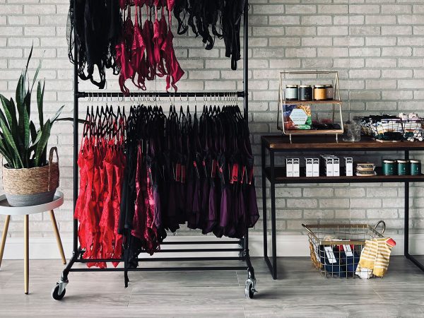 View of filled rack of clothes alongside stocked shelves against at a brick wall at a boutique