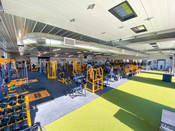 interior of a gym filled with a wide assortment of fitness equipment that is orange and silver colors with part of the ground covered in artificial short turf