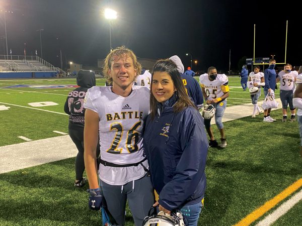 a women stands by her son in his football uniform by the side of the football field