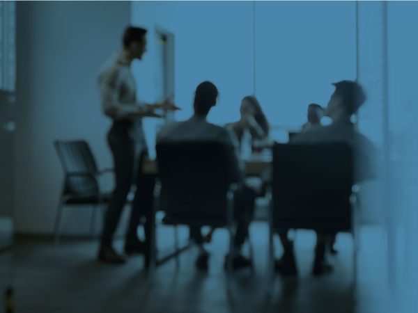 A blurry view of a group of people at a board meeting with one presenter speaking