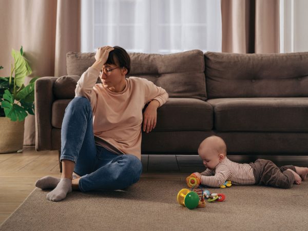 women resting in front of a couch on the floor with a baby playing besides her