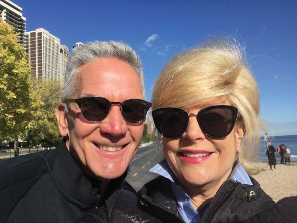 selfie of a couple on a beach both wearing sunglassses and black jackets