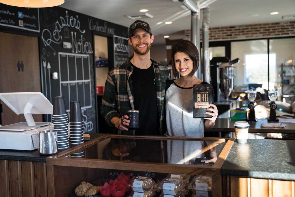 smiling at the camera. The man holds a coffee cup