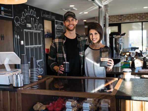 smiling at the camera. The man holds a coffee cup