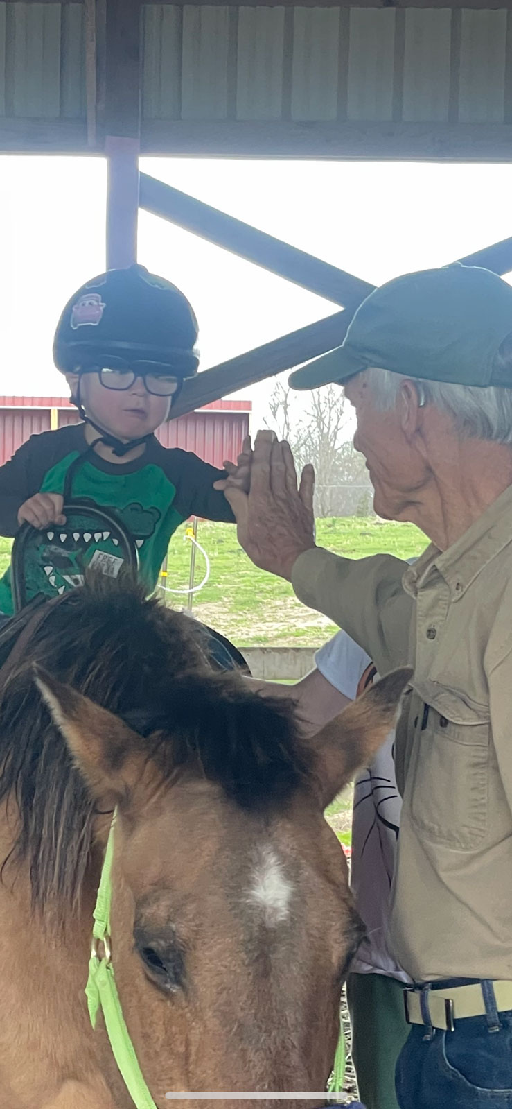 A young rider giving a high-five from the back ok a horse at Cedar Creek.