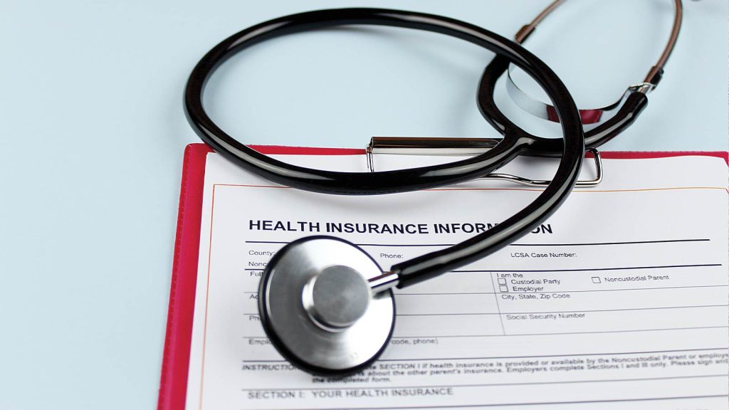A stethoscope rests on a clipboard with a health insurance information form. The form includes fields for details like the insured party and policy number. The background is a pale blue.