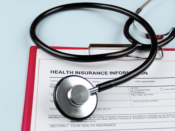 A stethoscope rests on a clipboard with a health insurance information form. The form includes fields for details like the insured party and policy number. The background is a pale blue.