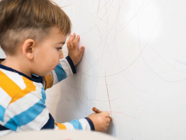 young Child Drawing On A Wall With Crayon