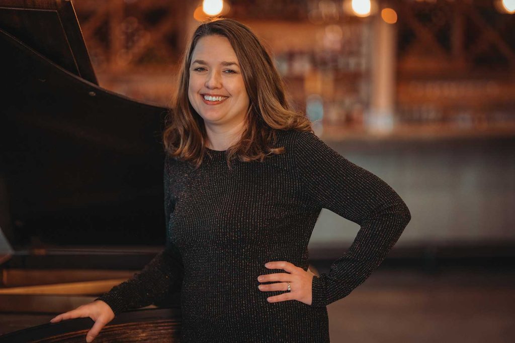 headshot of a women name Corrina Smith stnanding next to a black piano