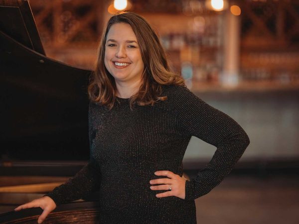 headshot of a women name Corrina Smith stnanding next to a black piano