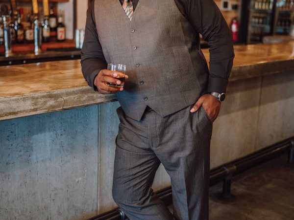 Headshot of a man named Darren Morton holding a whisky glass and standing besides a bar