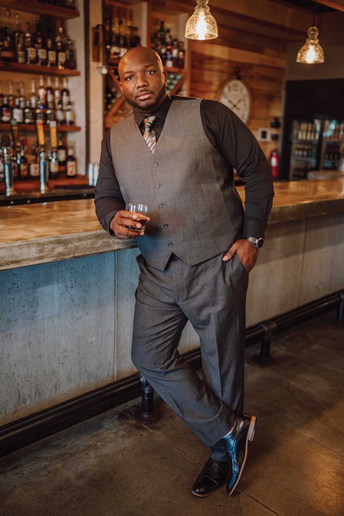 Headshot of a man named Darren Morton holding a whisky glass and standing besides a bar