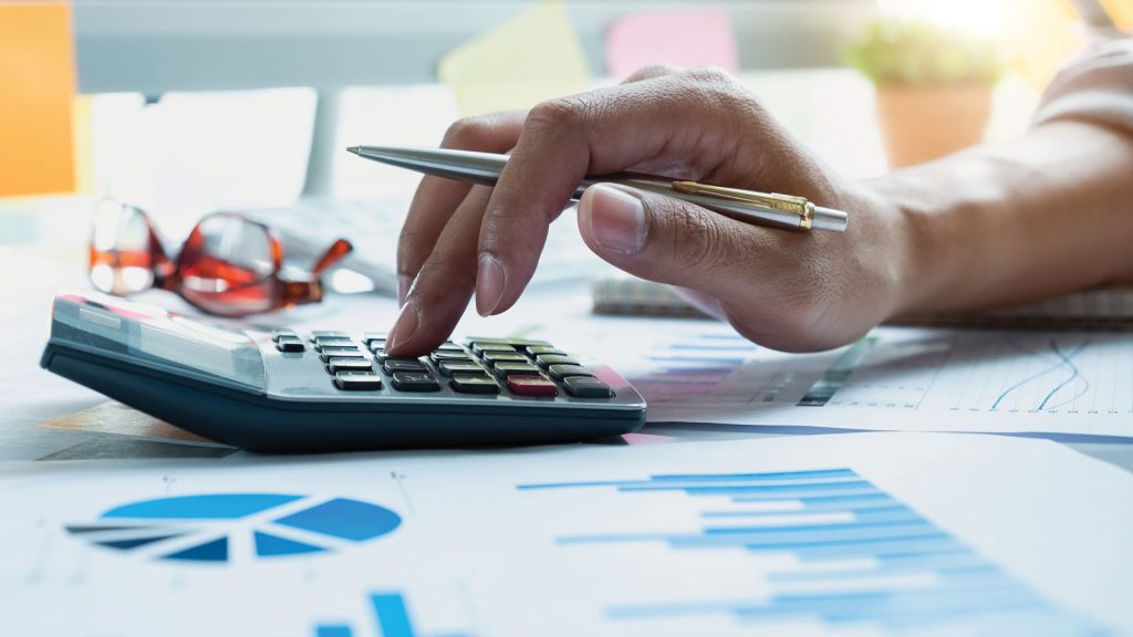 Fingers tapping a calculator surrounded by spreadsheets
