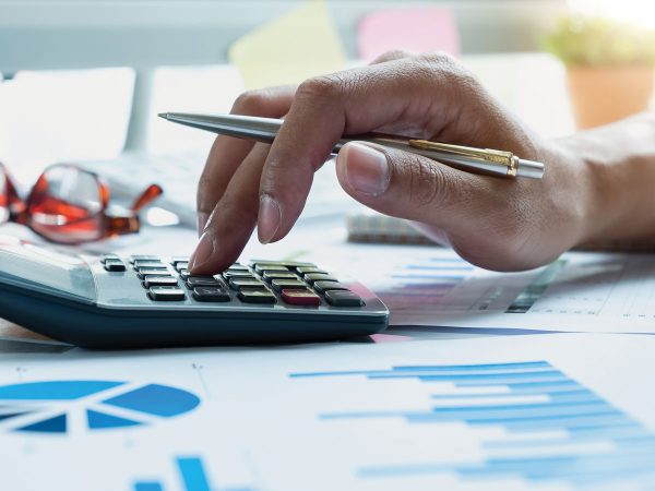 Fingers tapping a calculator surrounded by spreadsheets