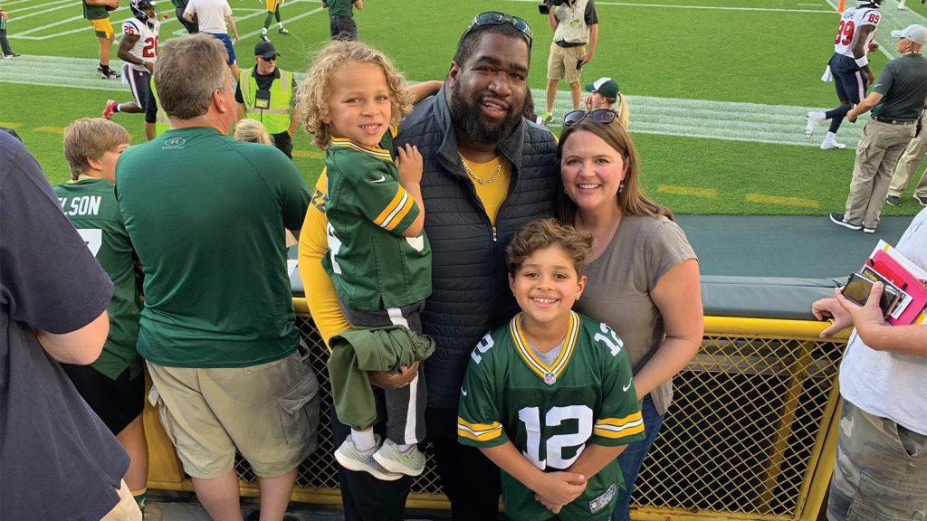 with the kids wearing green and yellow jerseys. People and players are in the background near the field. The atmosphere is cheerful and lively.
