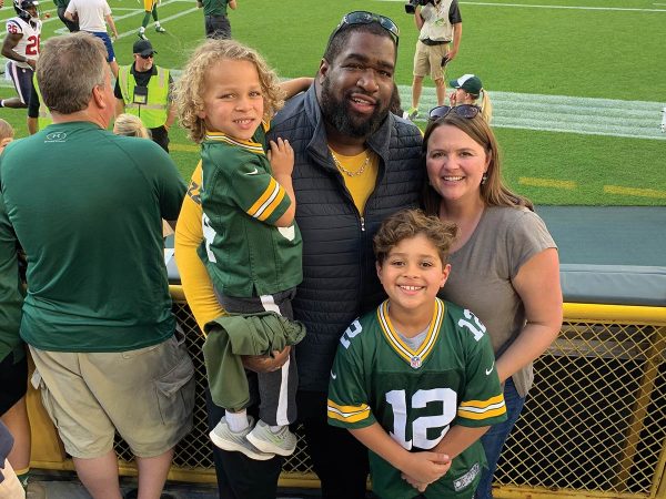 with the kids wearing green and yellow jerseys. People and players are in the background near the field. The atmosphere is cheerful and lively.