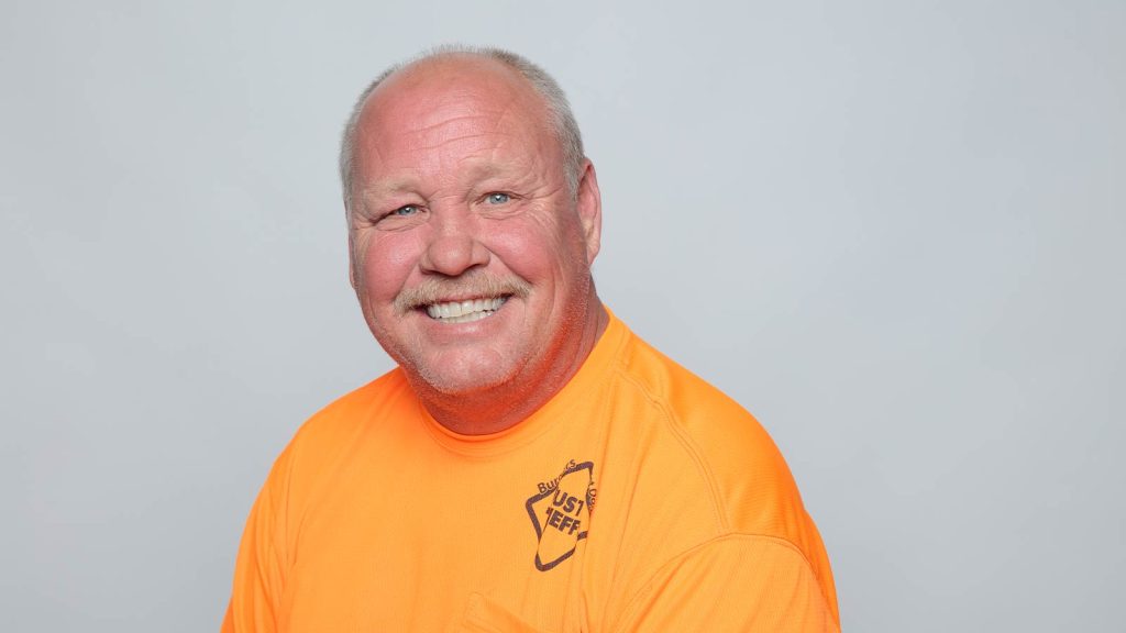 Smiling man in a bright orange shirt with text Just Jeff.