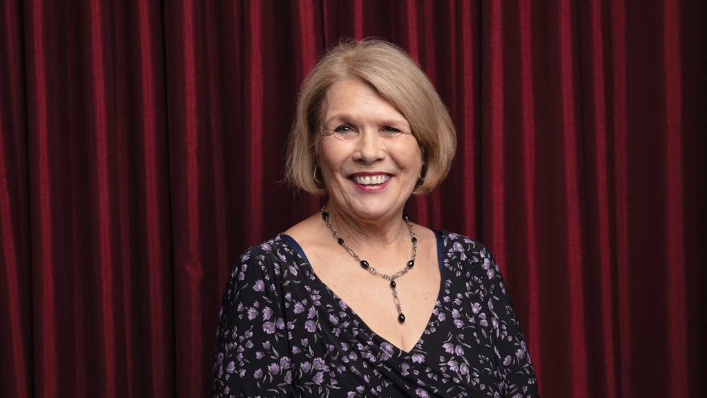 standing in front of a maroon curtain.