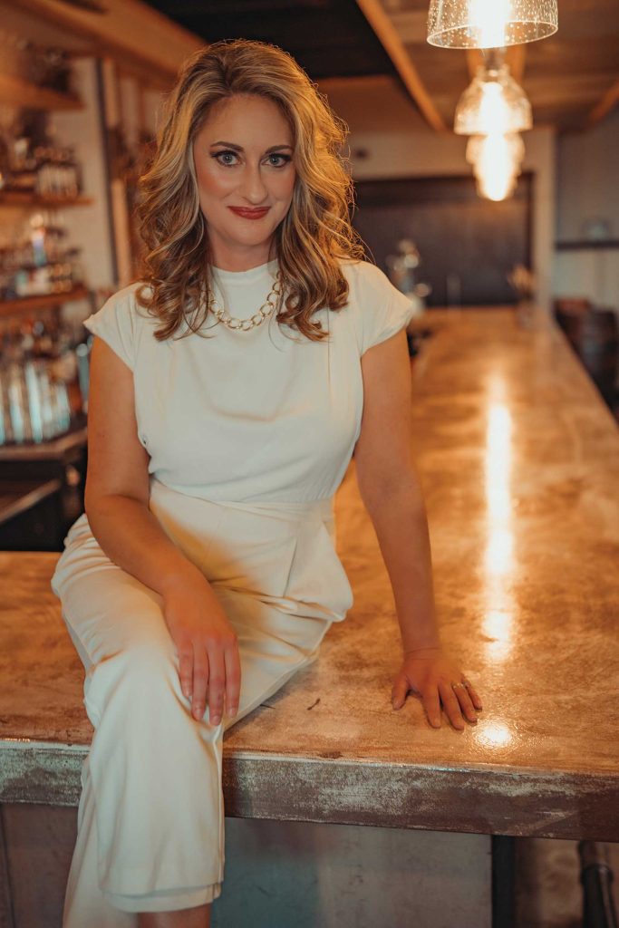 Headshot of a women named Megan Steen sitting on a bar counter top