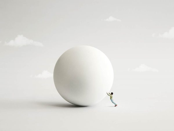 Surreal image of a small man attempting to push a large white ball on a grey surface with illustrative clouds in the background