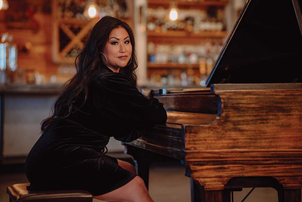 Headshot of a women named Ming Hsieh sitting on a piano bench in front of a piano