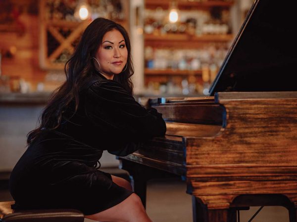 Headshot of a women named Ming Hsieh sitting on a piano bench in front of a piano