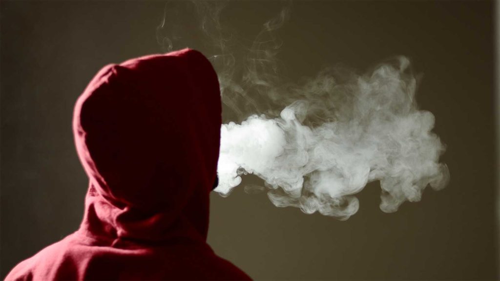contrasting with the hoodie and background. The image is focused on the vapor and the persons back.