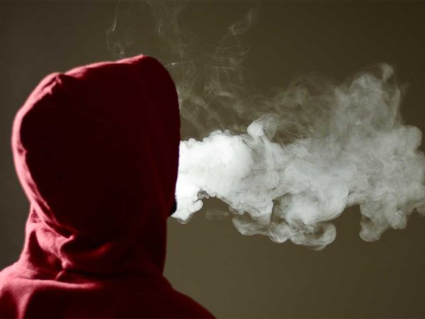contrasting with the hoodie and background. The image is focused on the vapor and the persons back.