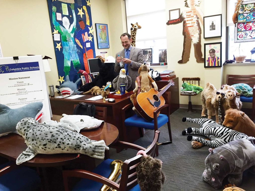 A man in a office surronded by large stuffed anumals