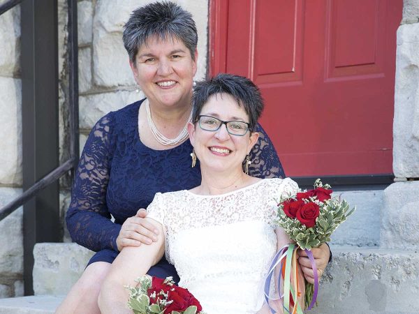 while the woman behind wears a navy blue lace dress. Both are smiling.