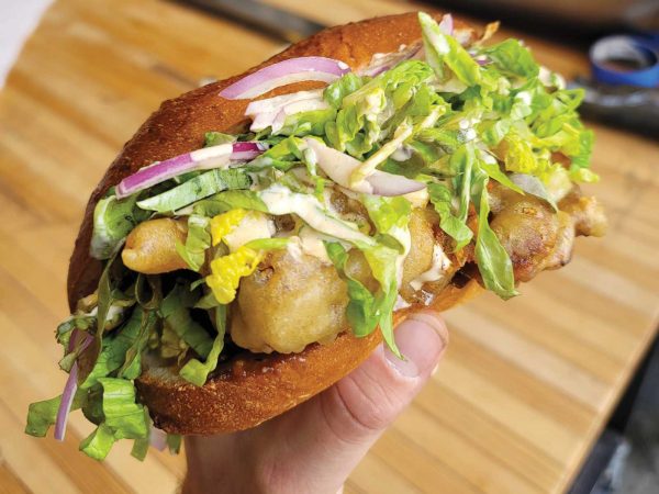 a hand holding a large sandwhich against a butcher block countertop