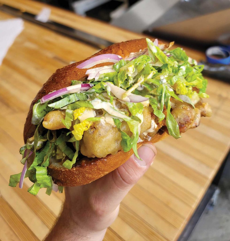 a hand holding a large sandwhich against a butcher block countertop