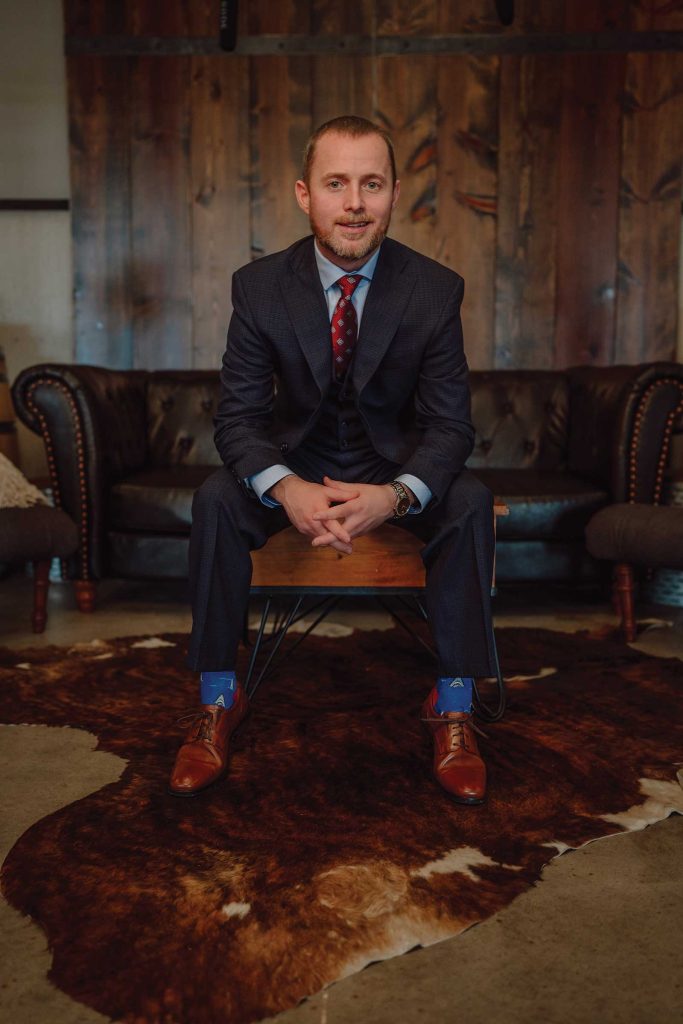 Headshot of a man named Tyson Mutrux sitting on a coffee table with a black couch in the background