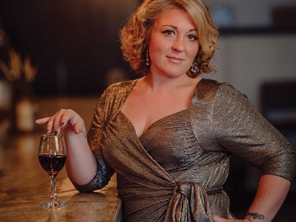 Headshot of a women named Wende Wagner standing at a bar with a glass of red wine