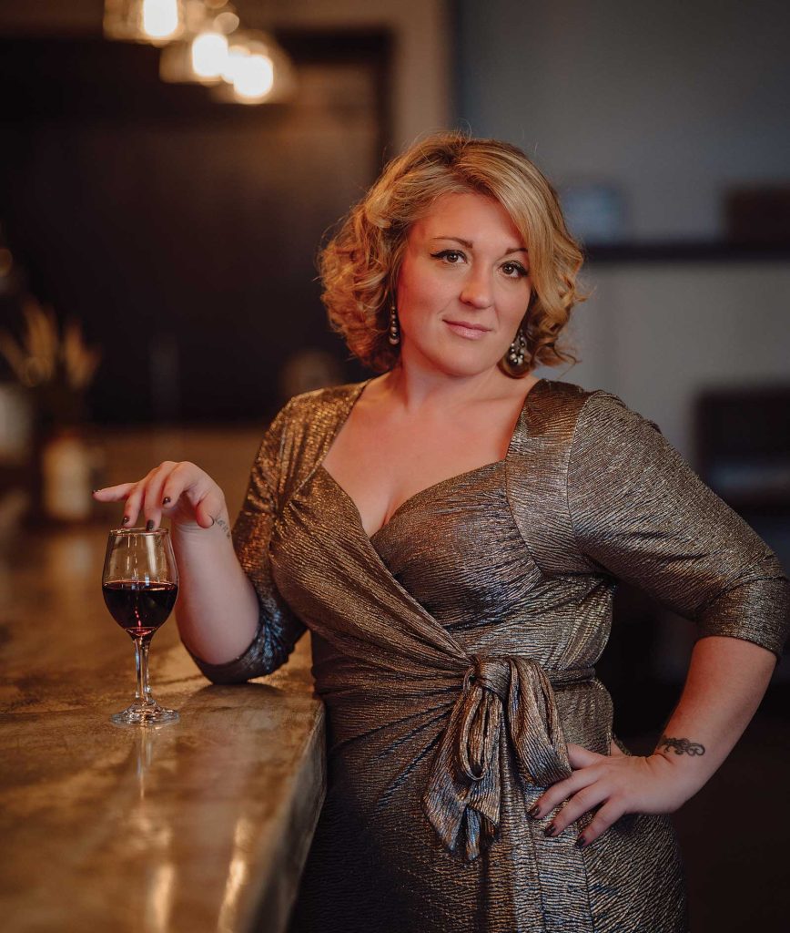 Headshot of a women named Wende Wagner standing at a bar with a glass of red wine