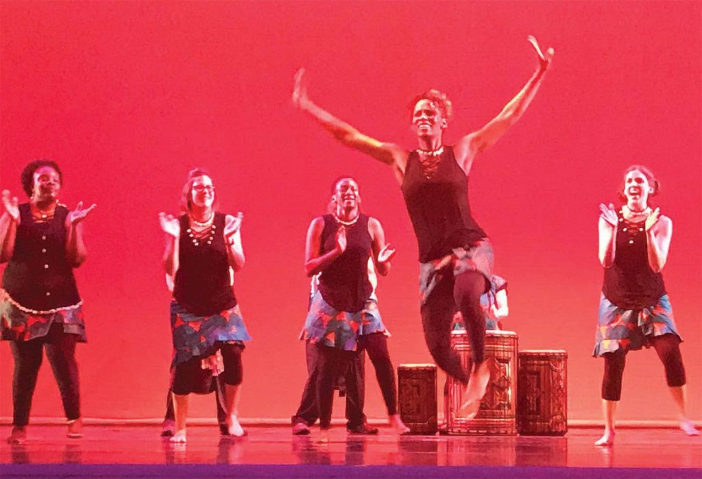 while others clap and smile. The background is illuminated in a warm red hue.