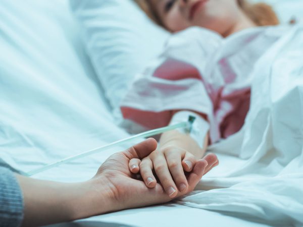 A-Parent-holding-the-hand-of-a-young-child-in-a-hospital-bed