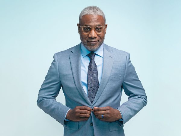 Jr. buttoning the front of his blue suit jacket standing in front of a blue background|A headshot of a man named Dr. Lester Woods