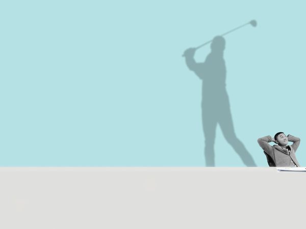 Man-sitting-at-desk-with-shadow-of-him-playing-golf-behind-him-wide