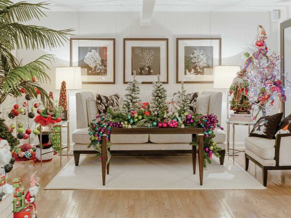 with a coffee table in front holding mini Christmas trees and colorful ornaments. Framed art hangs on the wall