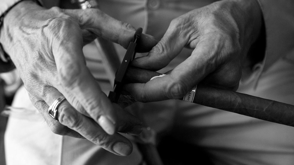 highlighting the texture and details of the skin and objects.|A person holds a lit cigar in one hand