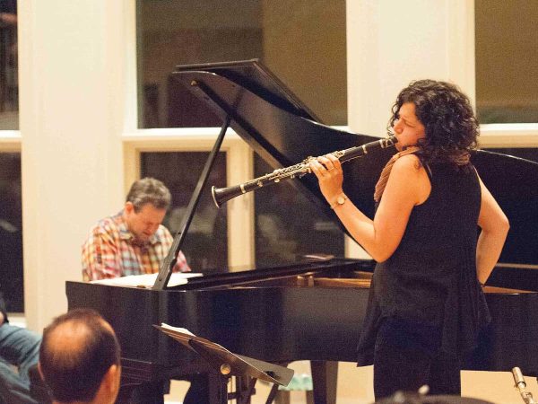 seated and attentive.|A pianist with long hair in a bun plays a grand piano on stage in a dimly lit venue. An audience sits at round tables in the foreground
